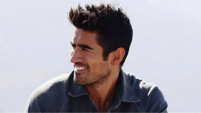 A smiling man with dark hair and a beard, wearing a collared shirt.