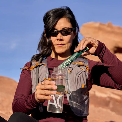 Woman pouring a green supplement stick into a water bottle.