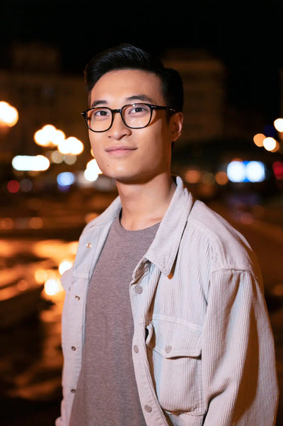 A young man wearing eyeglasses and a light-colored corduroy jacket over a grey t-shirt.