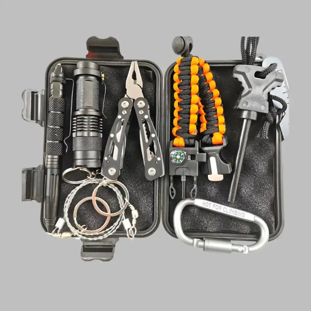 A black hard case containing various survival and outdoor tools, including a tactical pen, flashlight, multi-tool pliers, paracord bracelet with compass, fire starter, wire saw, and a carabiner.