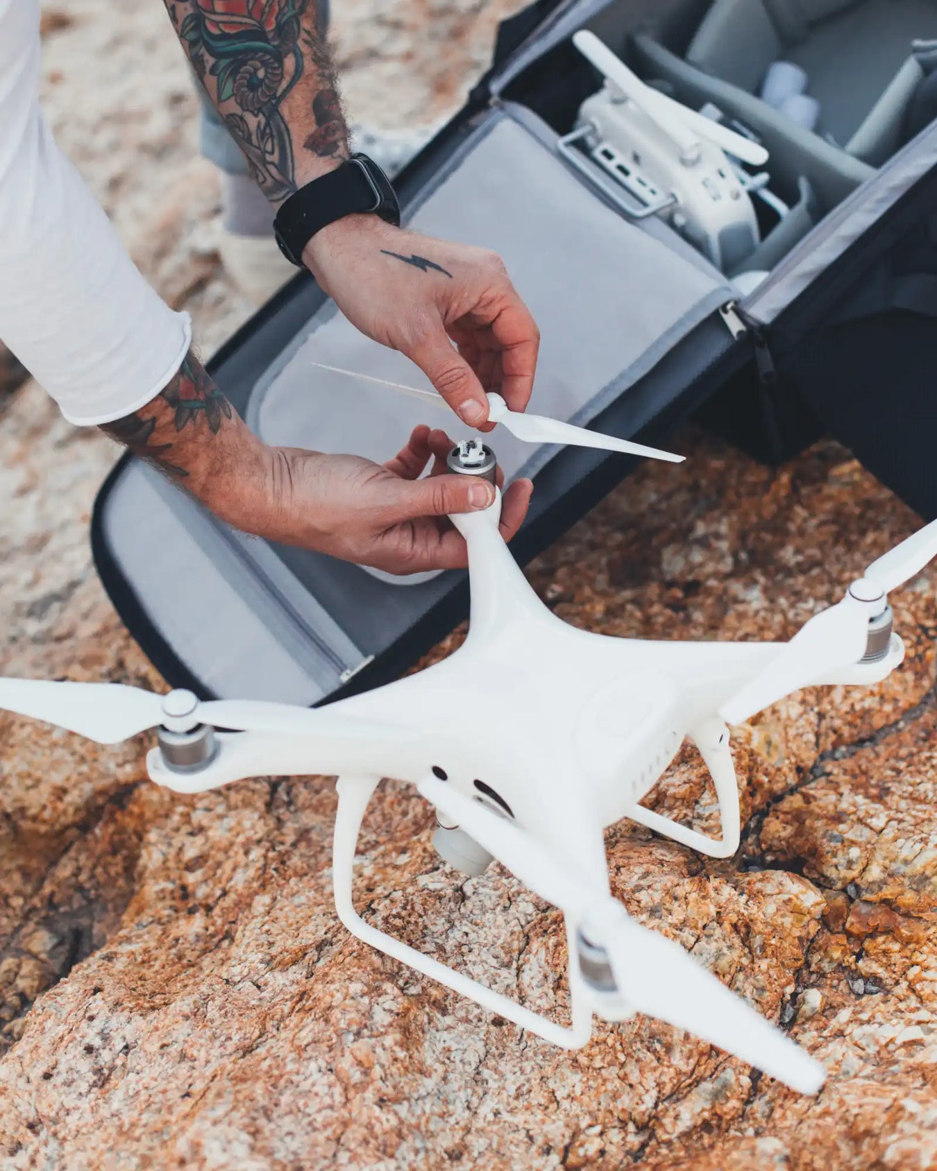 A person assembling a white drone by attaching a propeller, with a drone carrying case and controller visible in the background.