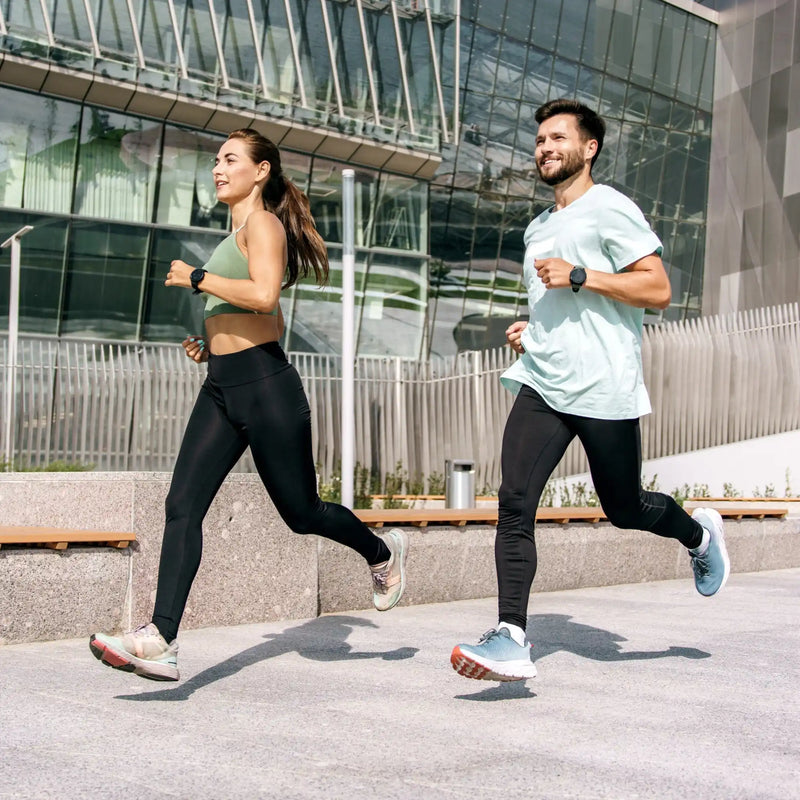 Two smiling people in workout attire running outdoors.